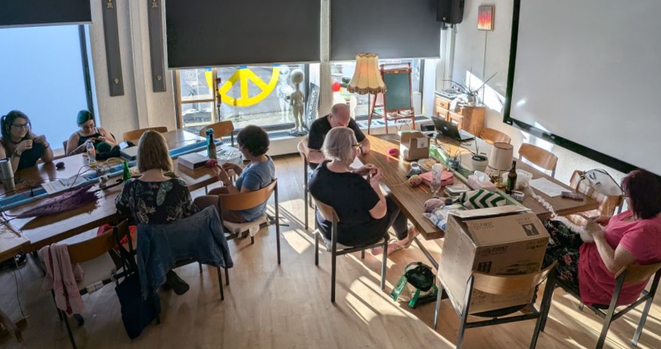 Zwei Tischgruppen im Hackerspace an denen 7 Teilnehmer des Häkeltreffs sitzen. Jeder häkelt an etwas anderem.