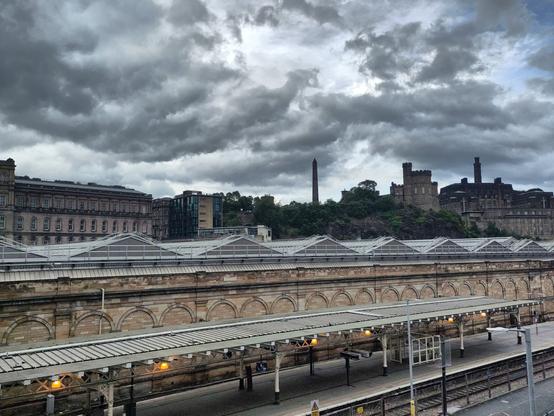 Beyond the roof of the train platform, the obelisk of the Political Martyrs Monument and the Castle, under a cloudy sky.