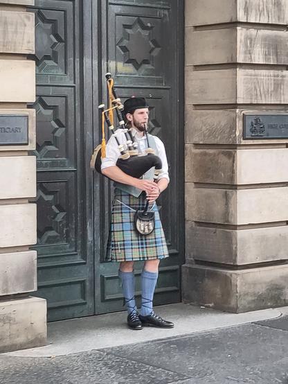 A bagpipe player in traditional cloths playing in the street.