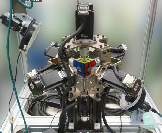 [ImageSource: Mitsubishi Electric]

Details about this particular robot:

•It is a camera, an industrial PC, a touch panel, and a 6-axis servo motor, connected to some very big sequencers, motion units, and servo amplifiers
•It can rotate its arms 90 degrees in 0.009 seconds
•It used "a color recognition algorithm that applies AI technology"
•Key to the robot was "high-speed signal connections and control between devices)
•The spinning ("winding") arms come from the team's experience in both home appliance and railway building, specifically making wire coils during motor manufacture
•AI worked to differentiate colors when positioning, shadows, or lighting might trip up a color sensor.