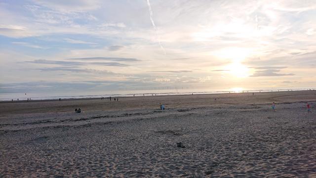 The end of a lovely summer's day, sun reflecting off the Irish sea as we look out across Crosby beach.  People are dotted across the sand and in the water and on the horizon you can just see the windmills of Burbo Bank offshore windfarm