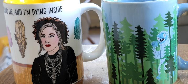 Moira Schitt saying and I'm dying inside, the other mug has the same forest with a blue large yeti-like creature looking out. These side would face the right-handed user