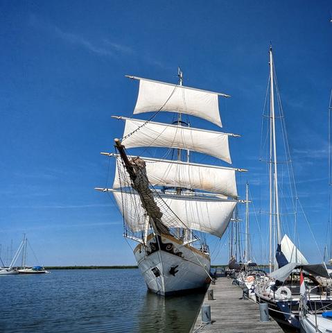 classic sailing ship moored at a jetty, the sails of the front mast unfurled