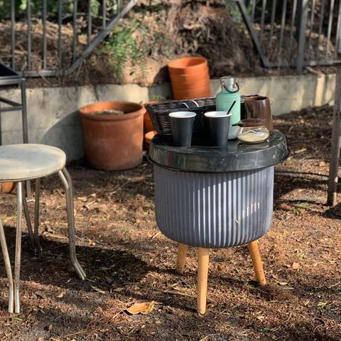 An op shop coffee service, and hot coffee in a vacuum flask on an improvised coffee table made from old planters, under a tree in dappled light.