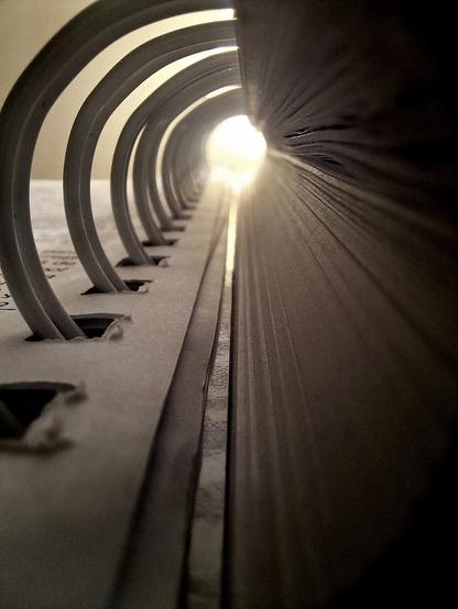 A close-up perspective of a series of metal arches arranged in a curve, creating an interesting visual effect as they recede into the distance. The focus is on the pattern and repetition of the arch design, with the light source at the far end creating a sense of depth.