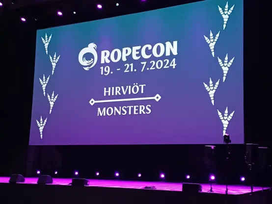 A stage with purple lights with text Ropecon with the date which was from 19th to 21st of July 2024, with monsters as a theme.