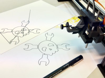 Two pen plotted versions of the Hackaday wrench and skull crossbones logo in black pen on white paper and card. One of them has pen plotted travel lines across it and the other one is complete. There is the black head of a pen plotter and a fineliner pen on the right of the image.