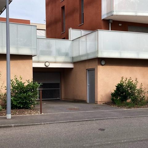 Une entrée de garage, appartenant à une résidence. Deux arbustes sur les côtés.
Les peintures du bâtiment forment un beau contraste.