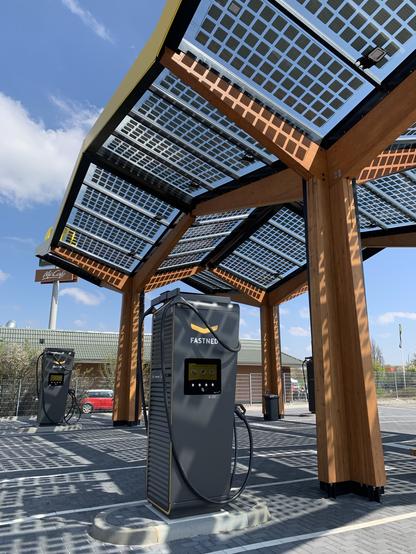 Electric vehicle charging station under a solar panel canopy on a clear day.