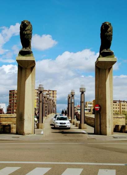 Front view of Lion statues at the Stone Bridge over Ebro river in Zaragoza. Aragon, Spain. There are cars on the bridge. Puffy a white clouds lining a Blue sky.