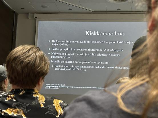 Slaidi Kiekkomaailma-luennolta, jossa alhaalla alaviite Pratchettin tapaan.
