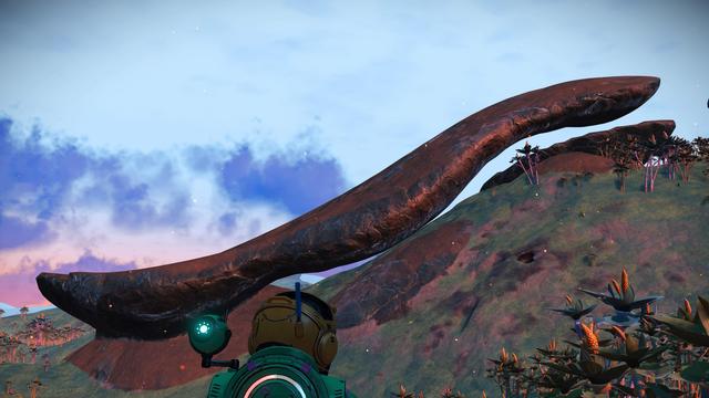 A screenshot from the video game No Man's Sky. We are looking at an alien planet's hillside. There is a rock formation anchored at the bottom which follows the curve up the hill, without ever touching it, forming a gentle S shape. The anchored end is larger and the whole thing looks like a spoon.