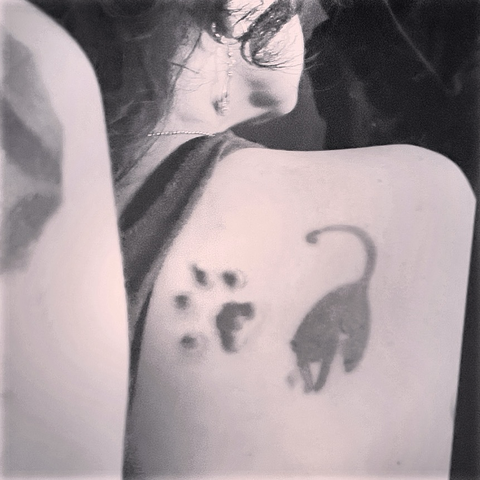 A black paw print tattooed next to a black cat on my back