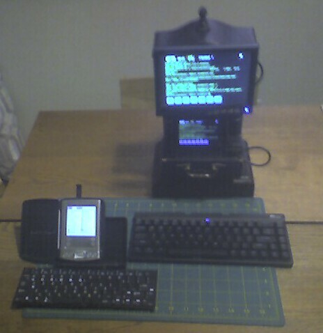 Here is a bad pic of my OCC setup taken with a Treo 680 PalmOS mobile. On the left is the palmOne Tungsten E2.  It is connected via infrared to the palmOne folding infrared keyboard.  
The Nokia N900 is on the right and is connected to the monitor with RCA video input.  I think the display is 7" and has other input options (HDMI, VGA, etc.)  I have it mounted on a repurposed broken clock.  Input device is the Royal Kludge folding keyboard connected via bluetooth.