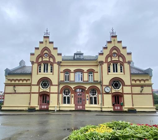 En vakker, lys gul murbygning med dyprøde tegninger. Den har runde og buede vinduer og to «tårn» med «trappetrinn».