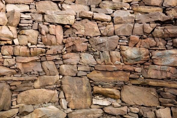 A colour photograph of the wall of Clachtoll broch in Assynt. Huge red sandstone blocks have smaller stones forming veins between them.
