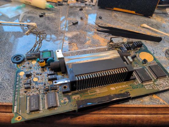 The back of a Sega Game Gear main board. The board has been removed from the console and is completely exposed. About half of the original electrolytic capacitors (large black square components) have been removed and replaced with fresh, high quality capacitors (cylinder-shaped, black, lying sideways).