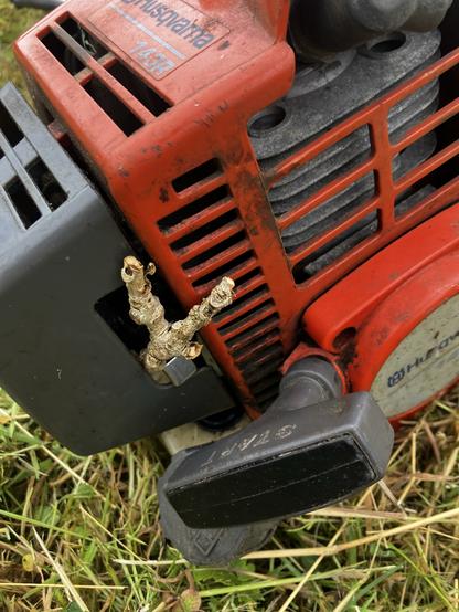 Close up of a strimmer / bushcutter engine. A small twig used to wedge the choke lever down to stop it riding up and closing off the air intake. 

One of three fixes to get the job done.
First job to flip the blade. Whoever put it on last, did so upside down making the non-cutting edge the ‘cutting edge’. 

The second was to clean off the spark plug, so it could actually spark. 

Then this to stop the choke choking and sputtering the engine to a stop ever two minutes.