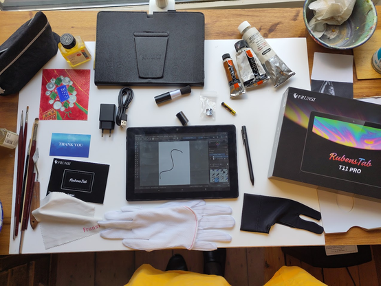 The Frunsi Rubenstab tablet with around it clockwise starting a 12 o'clock: tablet cover, lipstick-sized brush, brush cap, spare nibs and nib extractor, spare battery, pen, attracive box, black two-finger glove, white two five finger glove, manual, thank-you card, usb charger, usb cable.

Around the tablet stuff are brushes and paints. Those are not included.