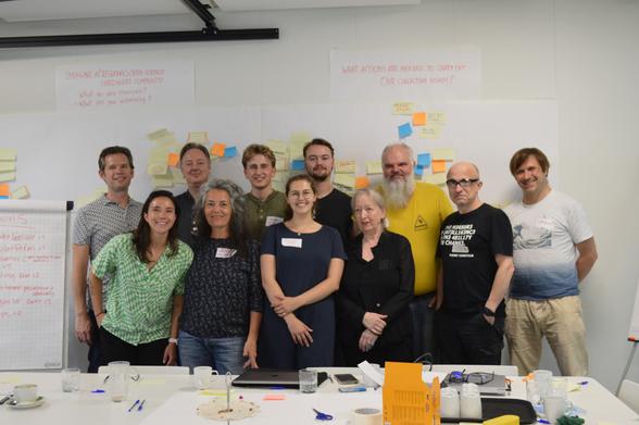 A group of GOSH attendees stand in front of boards full of brainstorming notes.