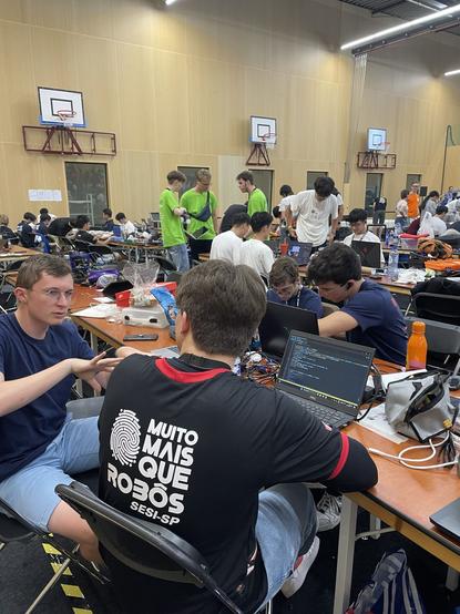 4 membres de l'équipe en plein travail sur leurs ordinateurs et robot en premier plan. En arrière pan, de nombreux autres jeunes en train de travailler.