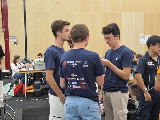 4 membres de l'équipe en pleine discussion. Au premier plan on aperçoit Clément Trouvé, le capitaine de l'équipe, portant le t-shirt de l'équipe inscrit de son nom et des sponsors régionaux de FLS.