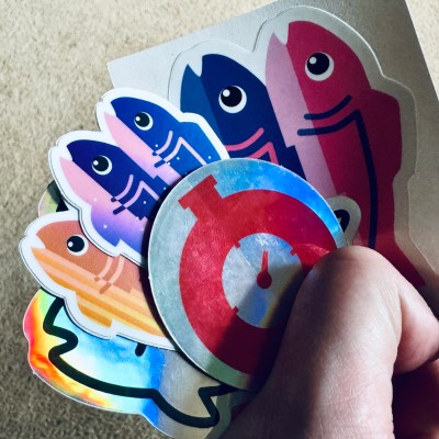 A hand holding a number of colourful cartoon fish stickers