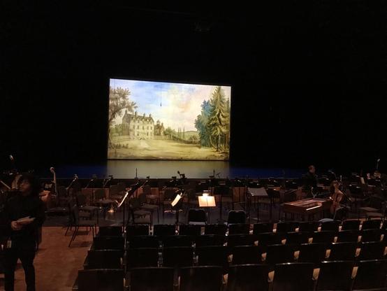 Space for the orchestra in front of a stage with a projection of an English manor house
