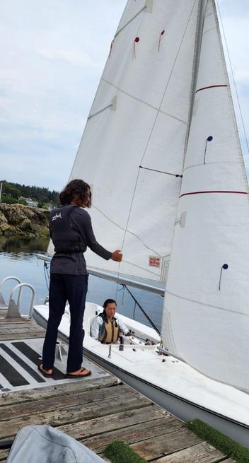 My young sailing instructor pulling on main mast. I'm in the sailboat.