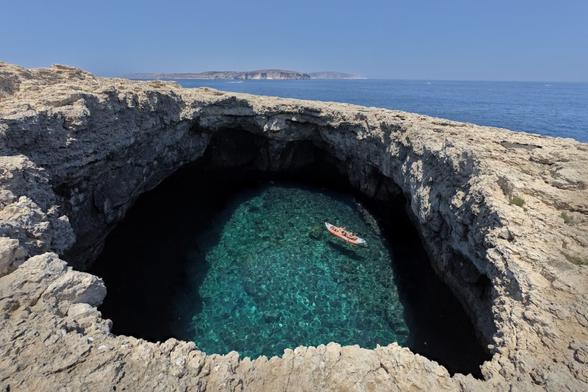 Un forat a la costa ple d'aigua, perquè està conectat al mar, amb una canoa dins.