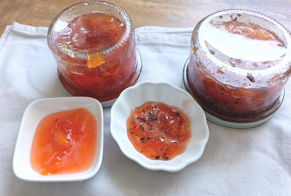 Auf einem Geschirrtuch stehen  2 Schälchen mit Marmelade, in einem sieht man die Lavendelblüten, dahinter 2 Gläser mit Marmelade auf dem Kopf stehend.