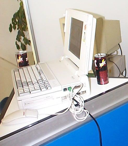 A really, really thick vintage laptop with detachable keyboard, tiny screen and ISA slot with an Ethernet card (10 MBit/s likely) and a connected PS/2 mouse.
