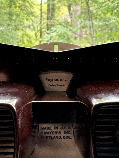 A close up of a brown View Master showing the window displaying the disc title which reads “Fog as in…”.