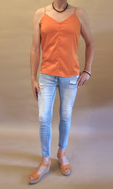 I’m wearing an orange camisole with pon pon “buttons”, stonewashed jeans and orange wedge heeled sandals. Seen from the front I’m also wearing a black pearl necklace and one black and one silver pearl bracelet on my left arm which I’m resting on my hip.