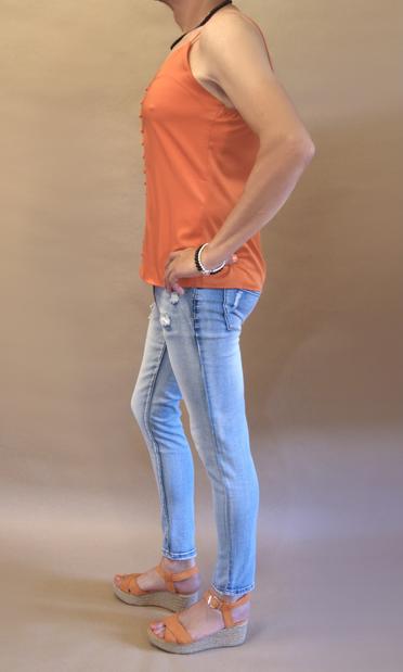 I’m wearing an orange camisole with pon pon “buttons”, stonewashed jeans and orange wedge heeled sandals. Seen from my left I’m also wearing a black pearl necklace and one black and one silver pearl bracelet on my left arm which I’m resting on my hip.