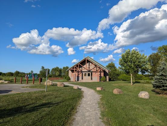 A lodge and walking trail under beautiful blue skies accompanied by fluffy white clouds.