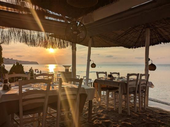 A photo of an outside taverna next to the beach with a sunset in the background