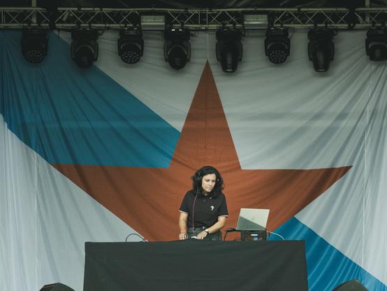Unha DJ pinchando nun escenario cunha bandeira da Patria xigante de fondo.