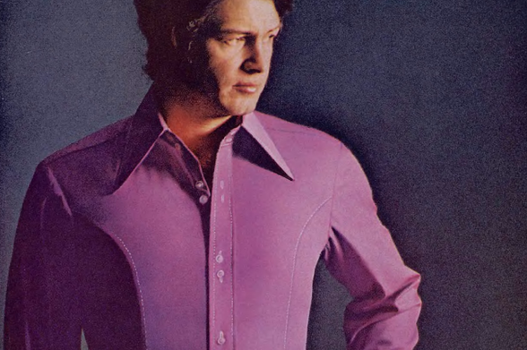 1970 Man in Pink Shirt

The image is a portrait of a man wearing a purple shirt.
He has short hair and is looking off to the side with a serious expression.
There is no visible text on the shirt itself, and the background is dark and out of focus, which highlights the man as the main subject.