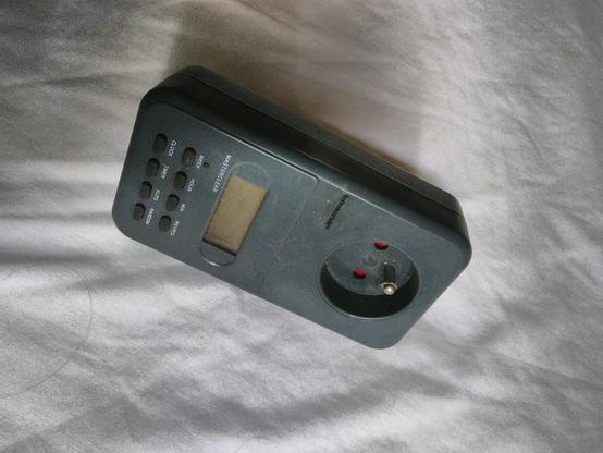 Prise électrique / programmateur électronique posé sur un drap. On peut voir l'écran LCD éteint.