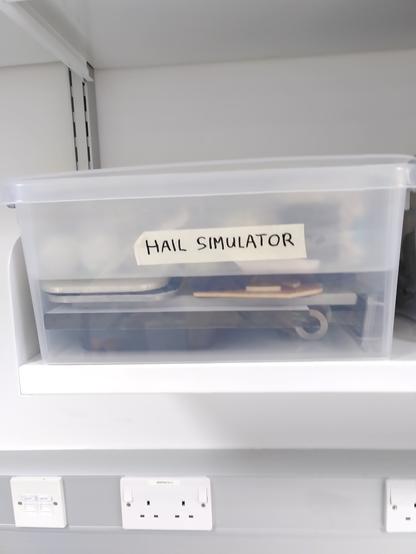 A plastic box of metal components labelled "Hail simulator". There is no indication of how the pieces fit together or what they would do if they did