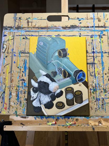 Painting on easel. Subject is a stuffed cow toy next to a film strip projector. The projector has a film strip in it and is turned on. The front of the projector is propped on a book and there are three metal film strip canisters.