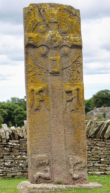 A photo of another roadside stone, showing what is possibly a hunting scene. The main carving is another cross but arrayed around it are knotwork and superbly intricate depictions of animals, although some of them are badly weathered.