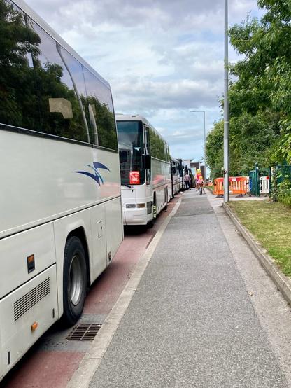Photo of a footpath beside a new dedicated cyclepath. The cyclepath is completely covered by parked busses forcing a family with a cycling child to use the footpath.