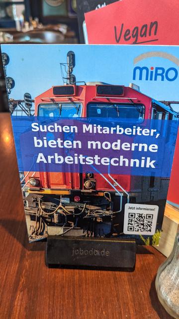 Werbekarte mit US-amerikanischer Diesellok im Hintergrund und dem Text "Suchen Mitarbeiter, bieten moderne Arbeitstechnik" im Vordergrund.
