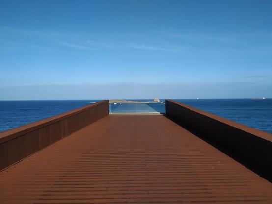Un mirador de color óxido se extiende hasta el mar, donde su final encaja perfectamente con el horizonte creando una composición simétrica.