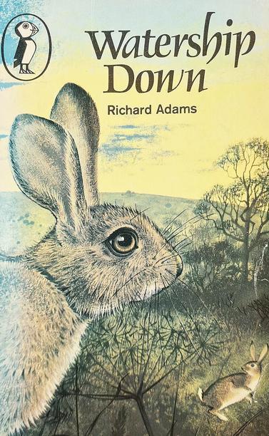 A very faded paperback book cover, mostly in pastel tones of yellow, green, and blue. A rounded, grassy hill in the background is backed by a cloudy sky with patches of blue in it. A single tree is halfway up the hill on the right. In the foreground, filling from the bottom left to near the top is a sad-looking rabbit facing to the right. Text in the space in the sky above its head reads "Watership Down" and "Richard Adams". The publishers' logo of a cartoon puffin in an oval is top left.