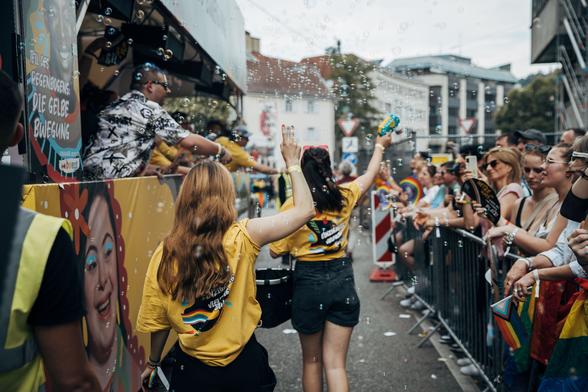 Menschen in gelben T-Shirts laufen neben dem bwegt-Paradewagen beim CSD in Stuttgart.