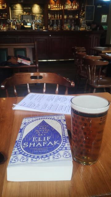 Copy of Elif Shafak 's There Are Rivers in the Sky next to a pint of ale in a Scottish pub