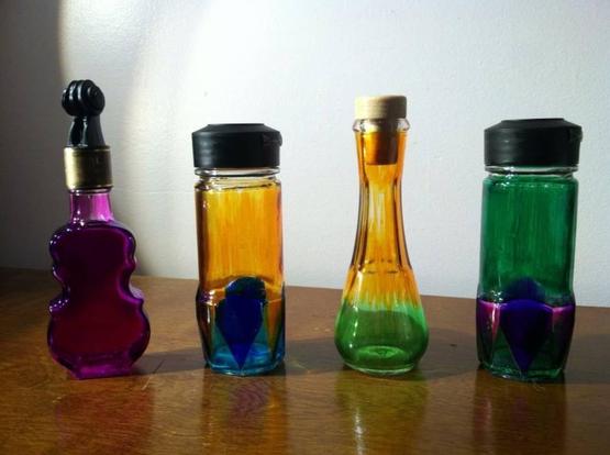 Four colorful glass bottles with various shapes and stoppers arranged on a wooden surface.
